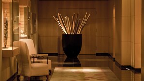 A modern lobby with a white armchair, a black vase with bamboo sticks, and a reflective floor.