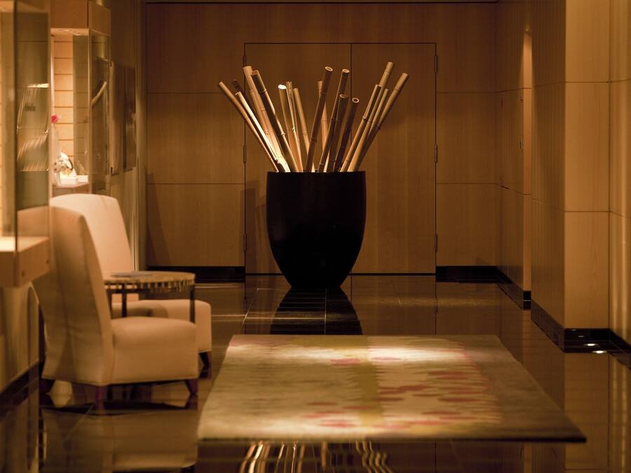 Un vestíbulo moderno con un sillón blanco, un florero negro con ramas de bambú y un piso reflectante.