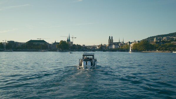A river with a boat in the foreground, buildings on the opposite bank, and a clear sky. - Park Hyatt Zurich (Zürich)