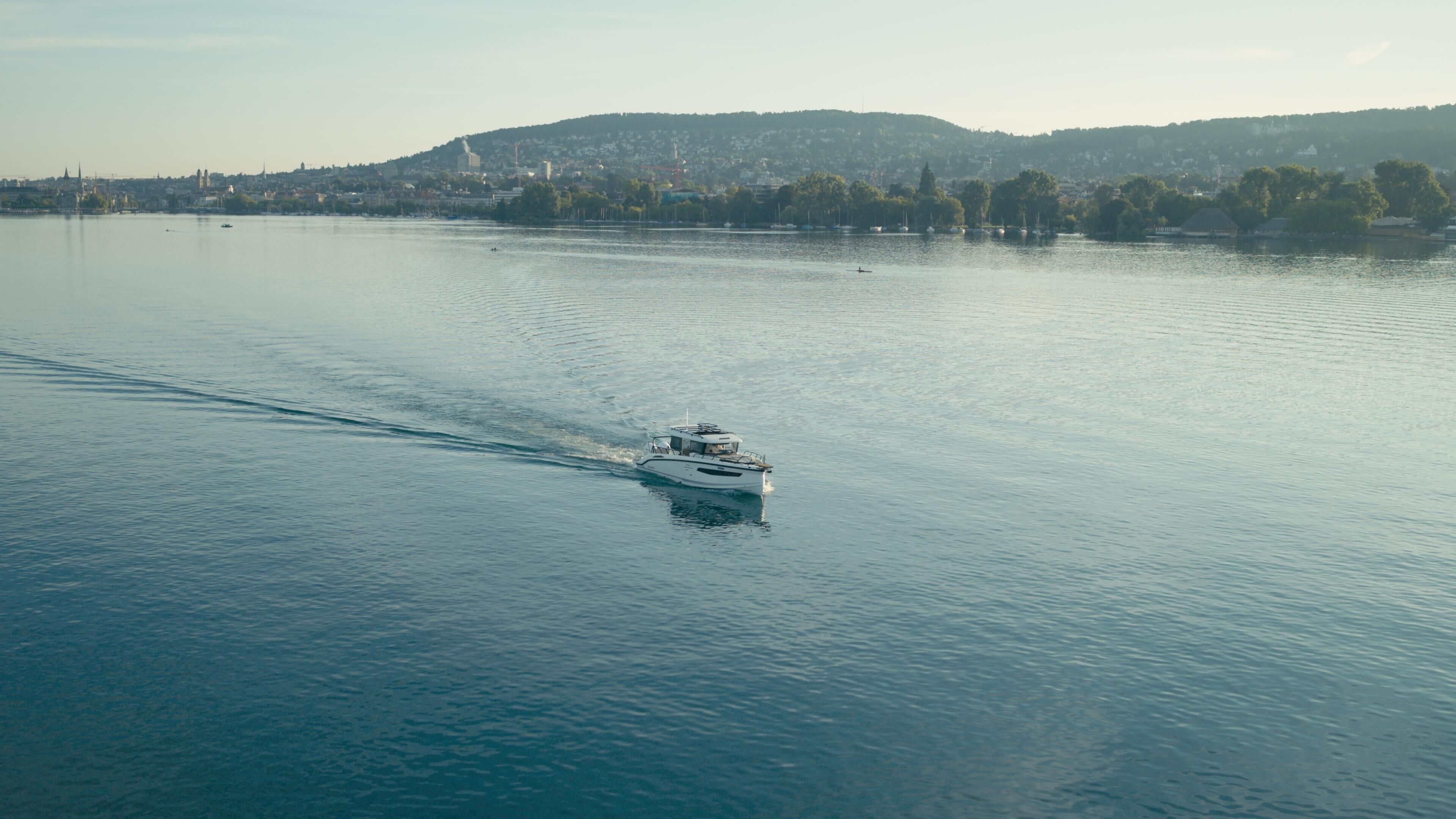 Un bateau sur une étendue d’eau calme, avec une vue lointaine sur une ville et des collines.