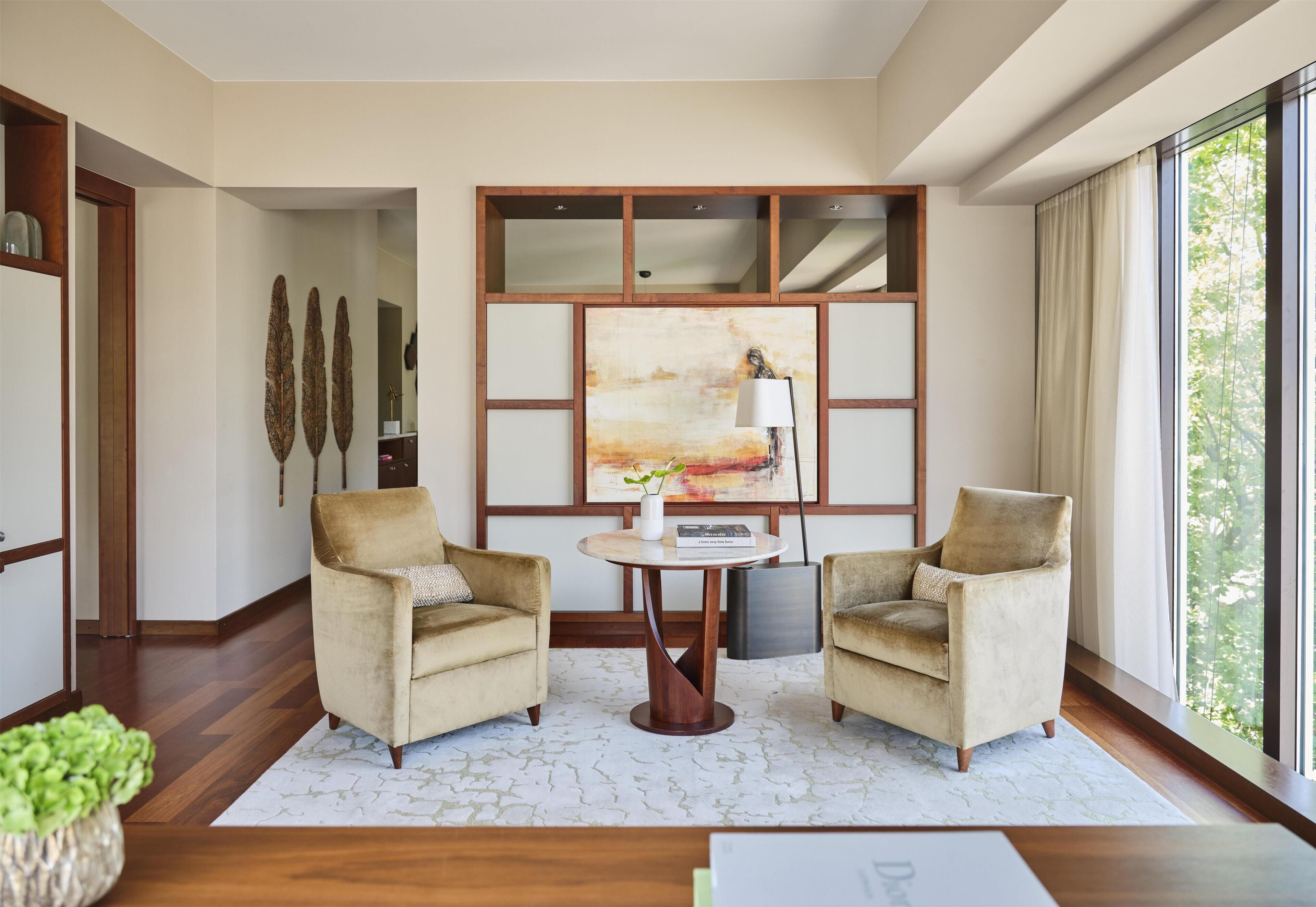Una habitación con dos sillones, una mesa redonda, un cuadro y un ventanal grande.
