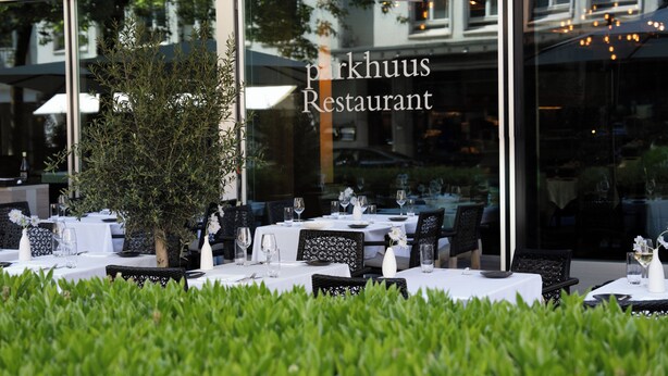 An outdoor dining area of Parkhuis Restaurant with tables set for two, surrounded by greenery and under umbrellas.