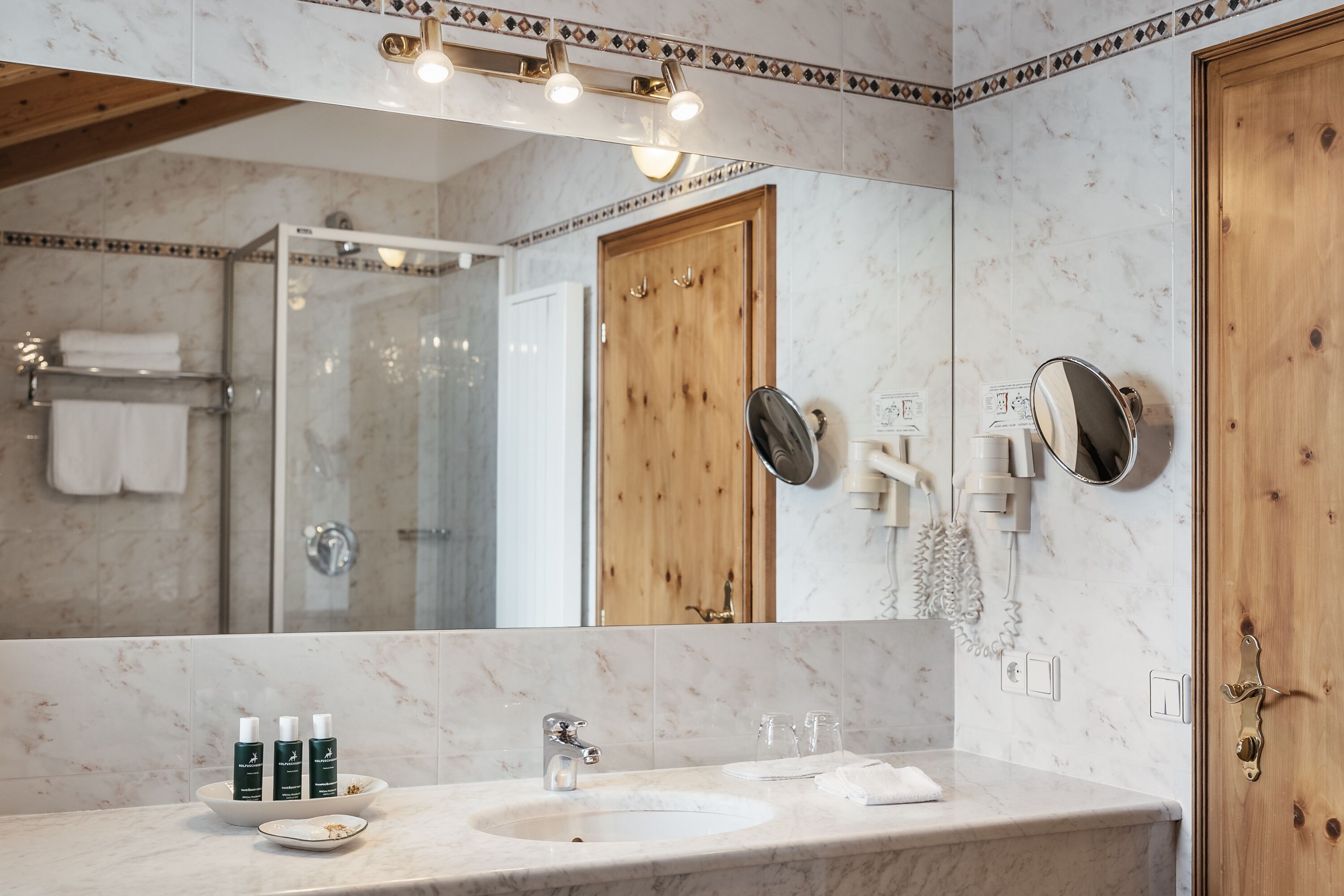 Un baño moderno con un lavamanos de mármol, un espejo grande y una puerta de madera.