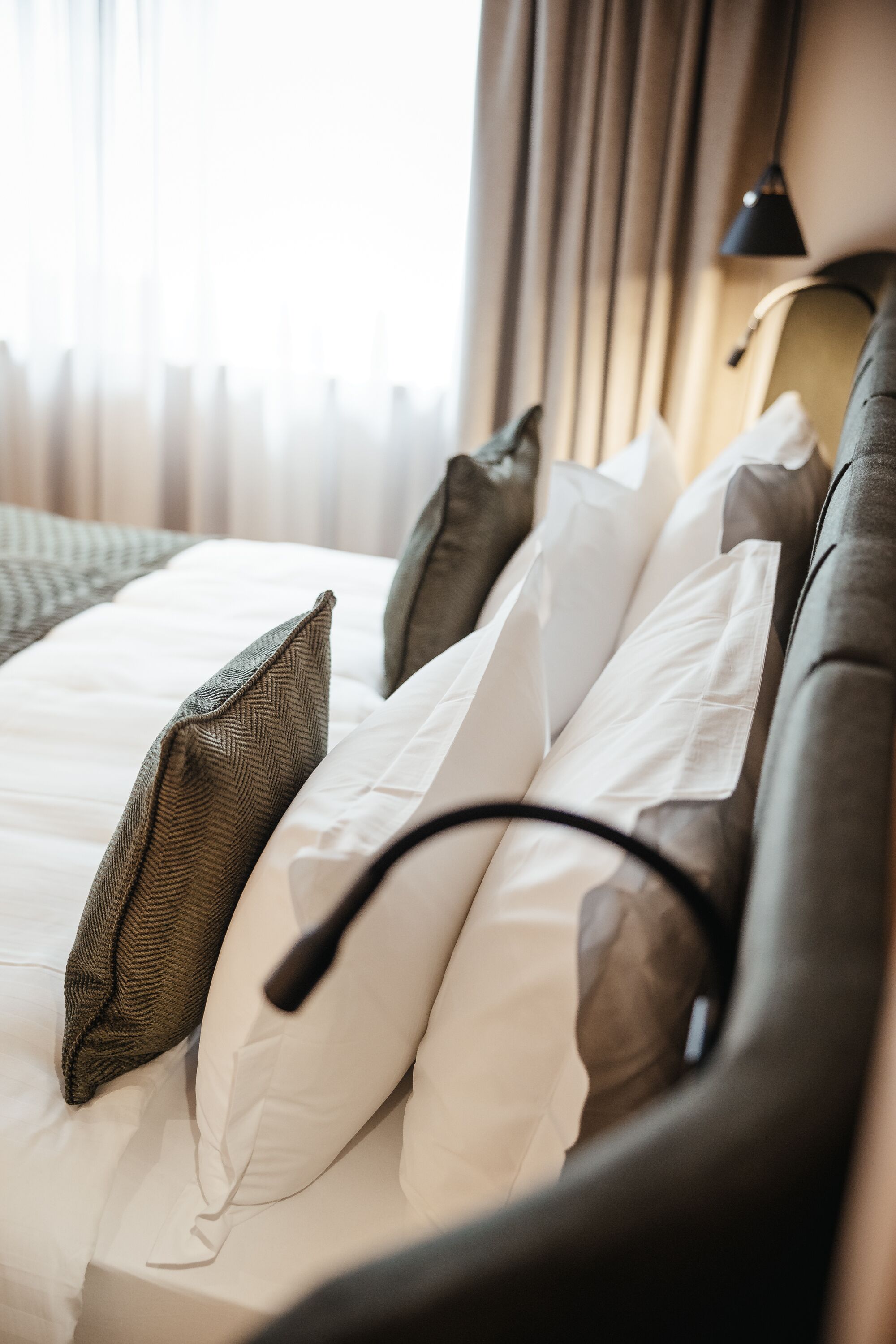 A neatly made bed with white and brown bedding, a black headboard, and a lamp on the wall.