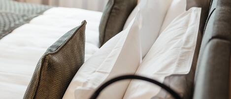 A neatly made bed with white and brown bedding, a black headboard, and a lamp on the wall.
