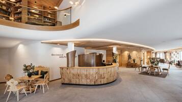 A modern hotel lobby with a curved reception desk, wooden bookshelves, and a seating area with tables and chairs.