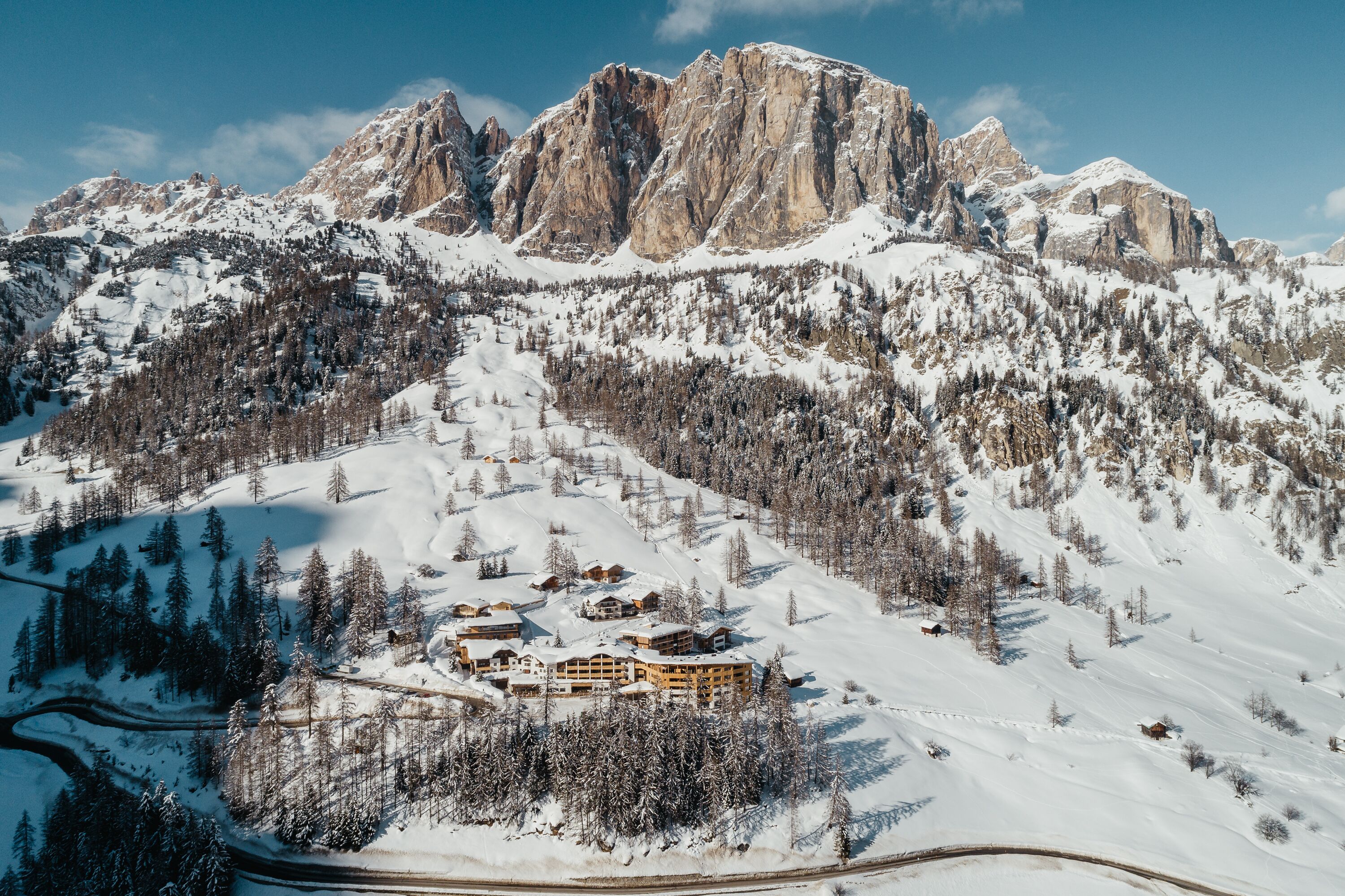 A snow-covered mountain resort with a prominent building surrounded by trees and rocky peaks.