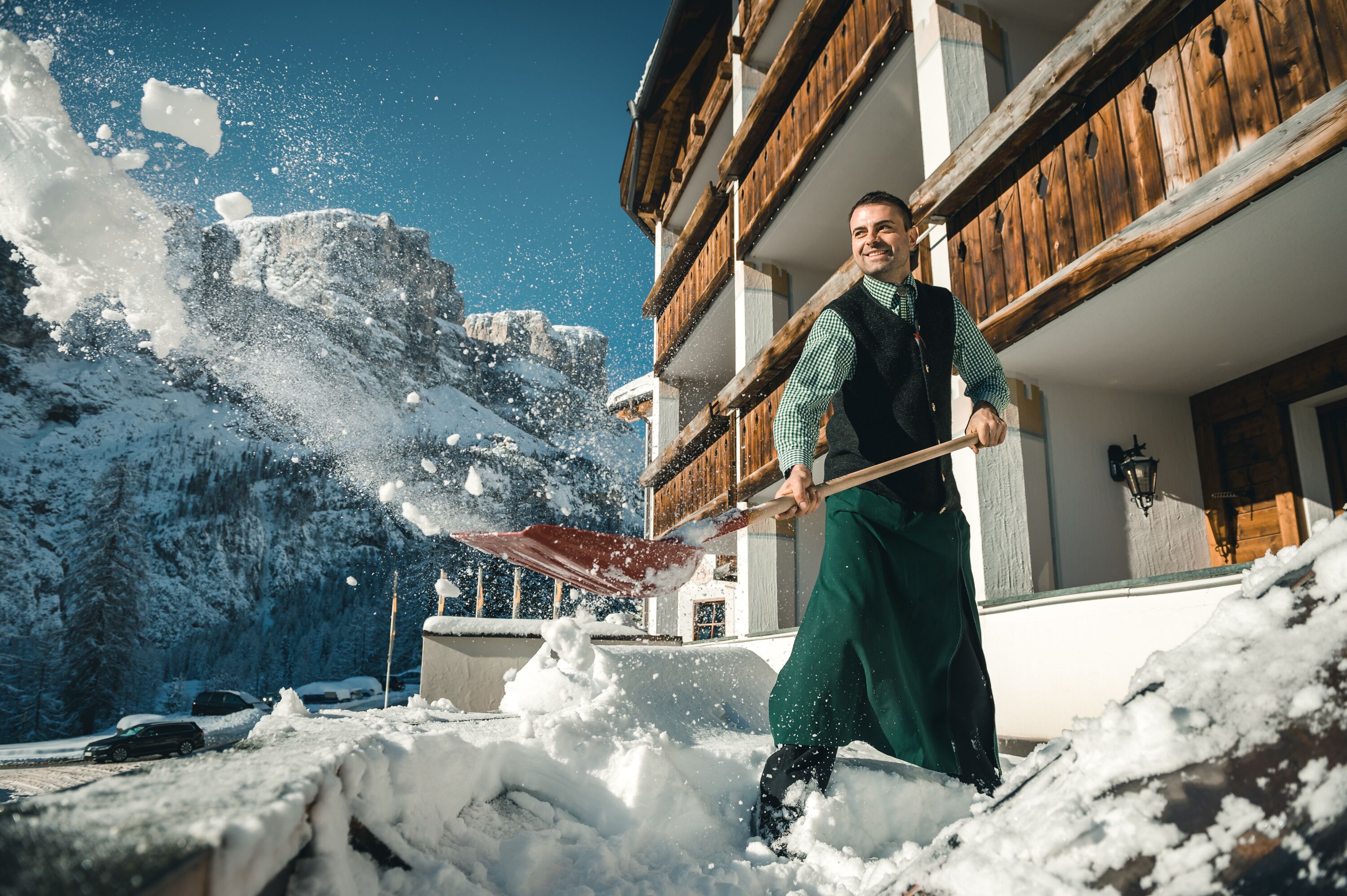A person shoveling snow in front of a wooden building with balconies.