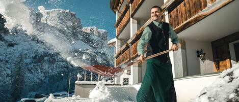 Una persona quitando nieve frente a un edificio de madera con balcones.