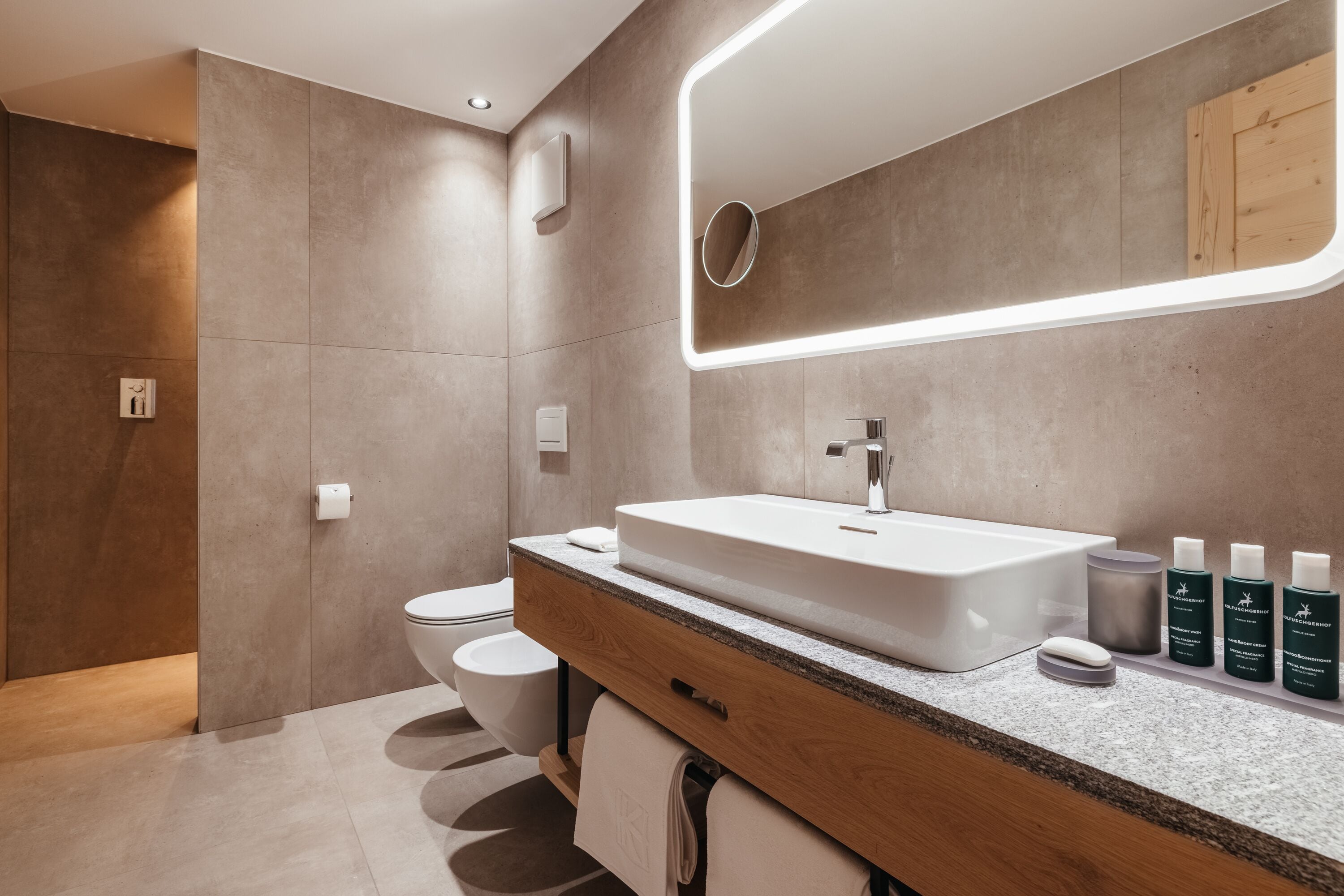 A modern bathroom with a large sink, mirror, and toiletries.
