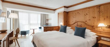 Habitación de hotel con una cama grande, cabecera de madera, mesitas de noche, un escritorio con silla y una ventana con cortinas.