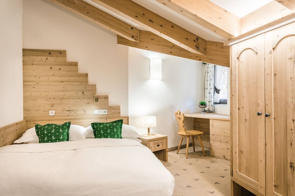 A bedroom with a wooden staircase, a desk with a chair, and a wardrobe.