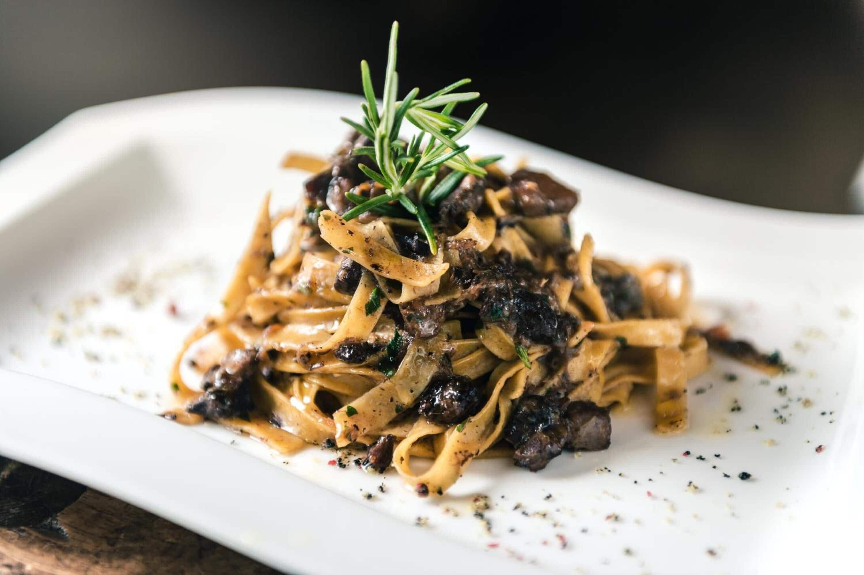 A plate of pasta with a sprig of rosemary on top.