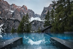 Un paysage de montagne avec un ciel dégagé, un chalet en bois et une piscine qui reflète les montagnes.