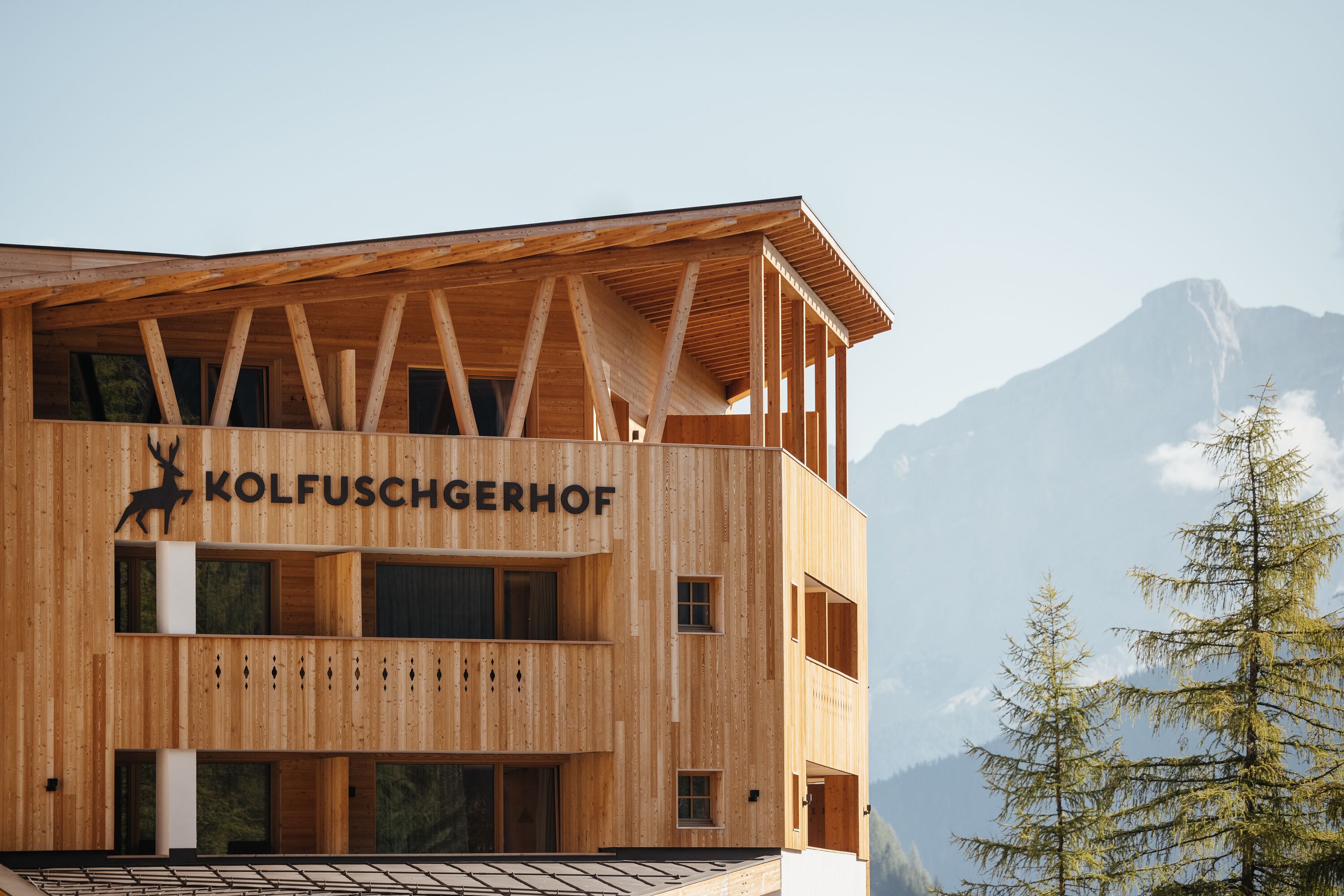 A wooden building with the name "KOLFUSCHGERHOF" and a deer logo. It has multiple windows and balconies.