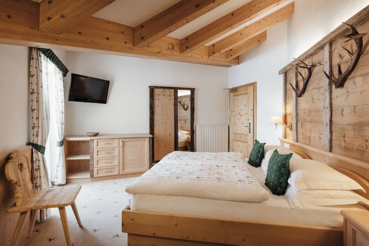 A wooden bedroom with a bed, a chair, a dresser, a television, and a wall-mounted deer antler decoration.