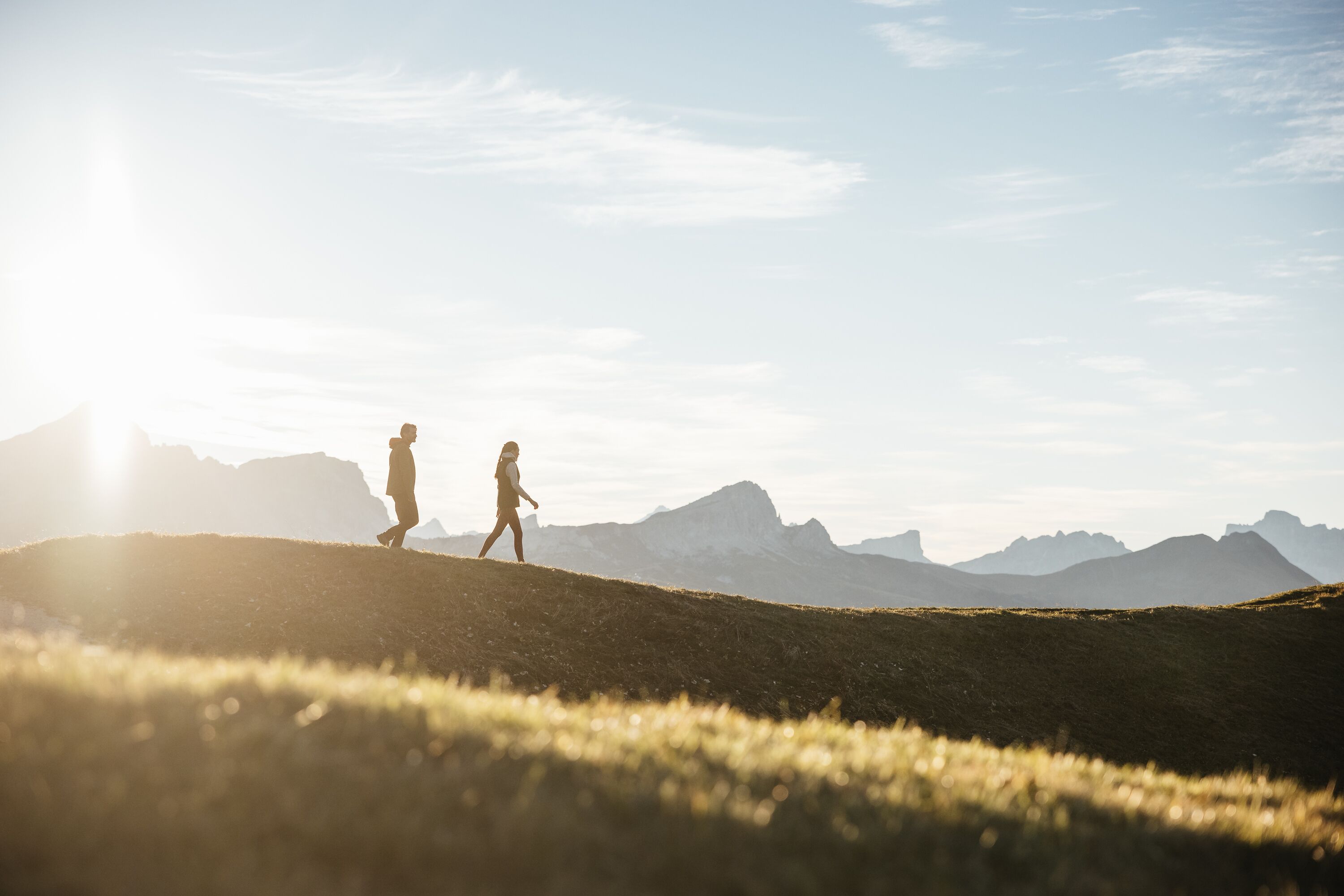 A person walking on a grassy hill with mountains in the background.