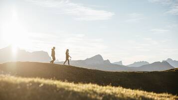 A person walking on a grassy hill with mountains in the background.