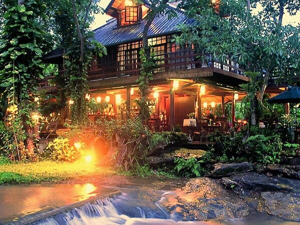 A traditional wooden building with a covered outdoor area, surrounded by lush greenery and a small waterfall. - Sukantara Cascade Resort & Spa (Mae Rim)