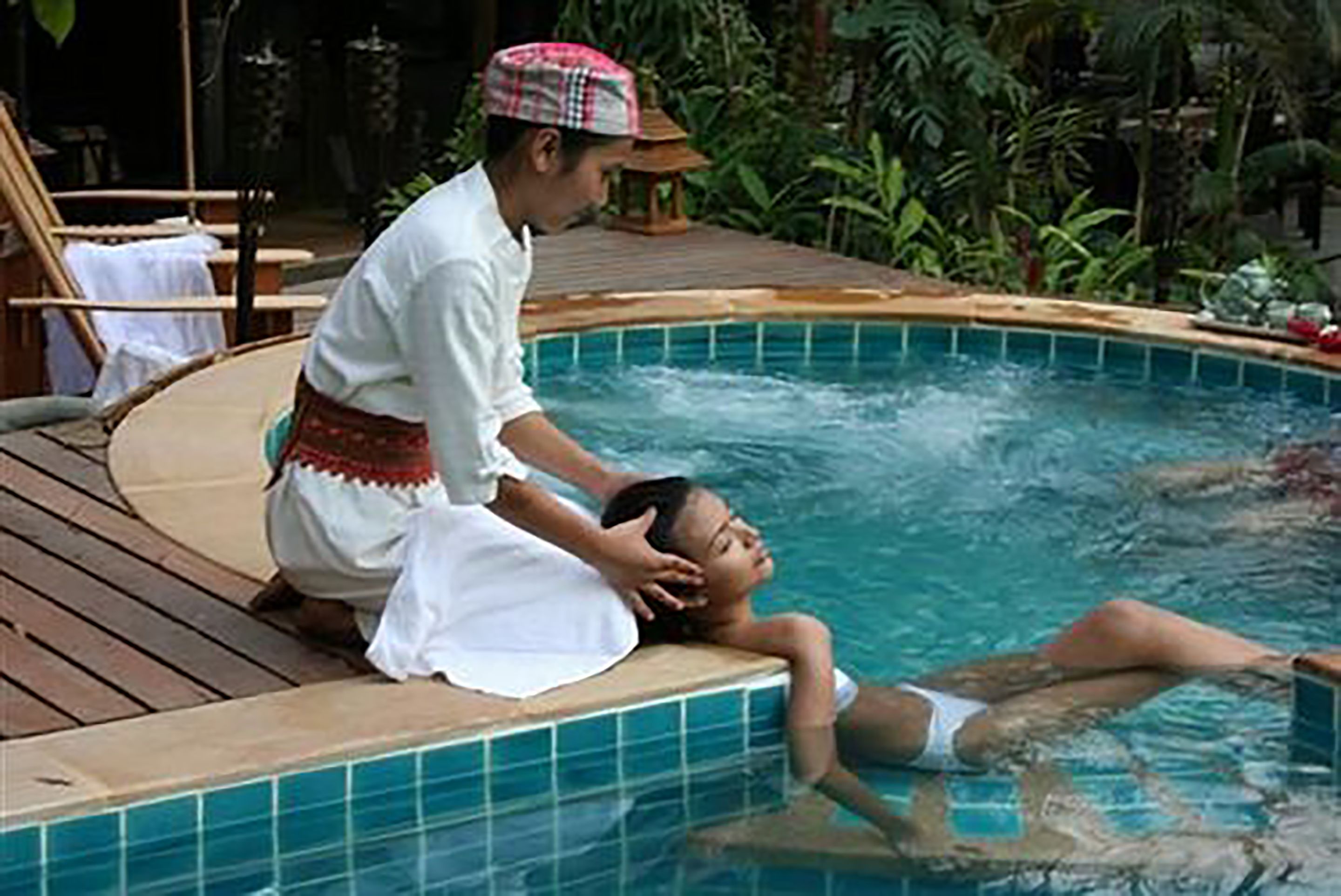 A person in a white shirt and traditional attire assisting another person in a pool.