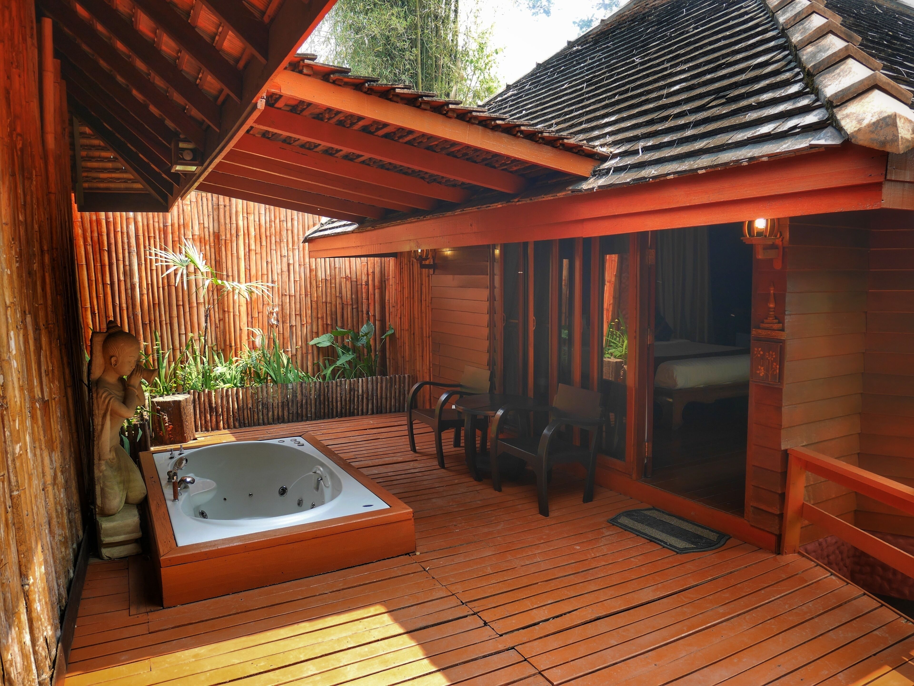 Terraza de madera con jacuzzi, pared de bambú y zona de estar.
