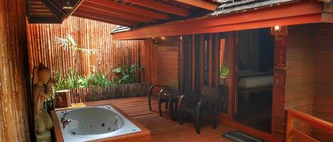 Terraza de madera con jacuzzi, pared de bambú y zona de estar.