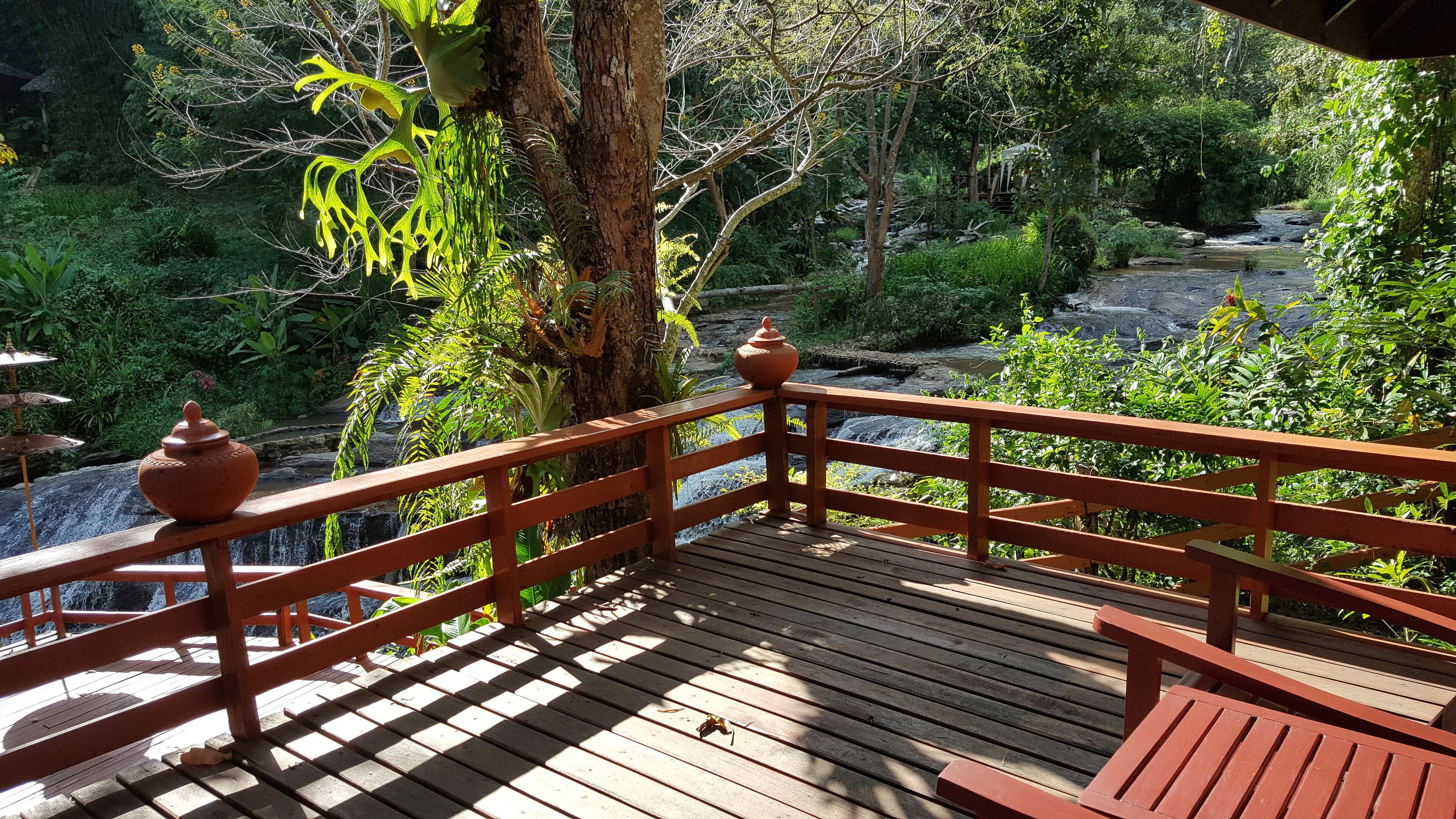 A wooden deck with a railing overlooking a garden with a waterfall.