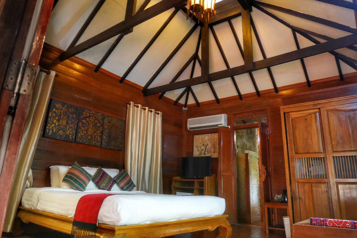 A room with a bed, wooden beams, a ceiling fan, and a window with curtains.