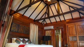 A room with a bed, wooden beams, a ceiling fan, and a window with curtains.
