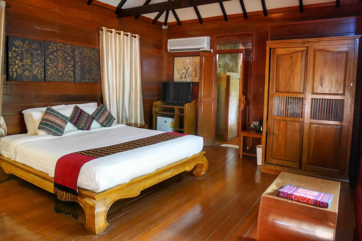 A wooden-framed bedroom with a bed, curtains, an air conditioning unit, and a wardrobe.