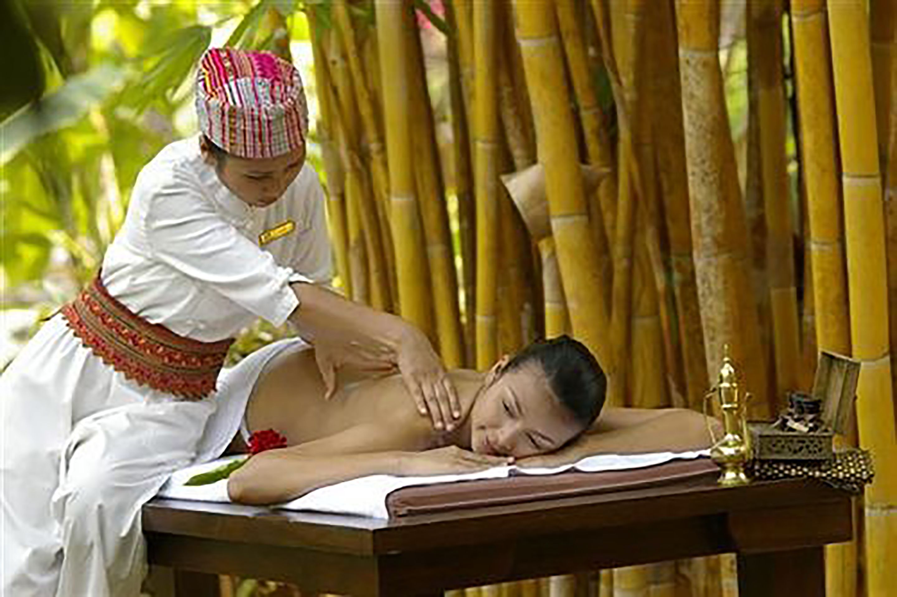 Une séance de massage dans une pièce aux murs en bambou et équipée d’une table de massage en bois.