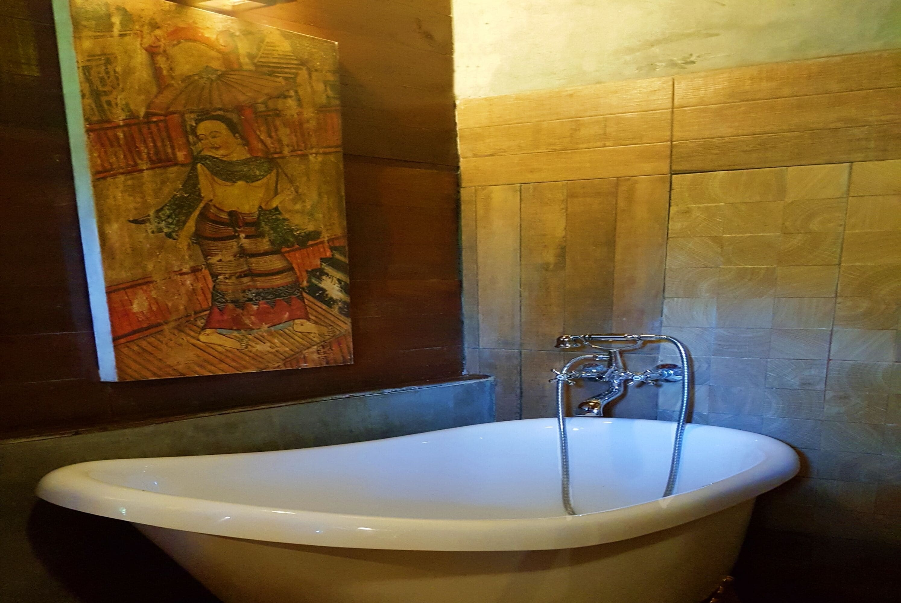 Une salle de bain avec une baignoire sur pieds, un lavabo fixé au mur et une fresque représentant une scène traditionnelle.