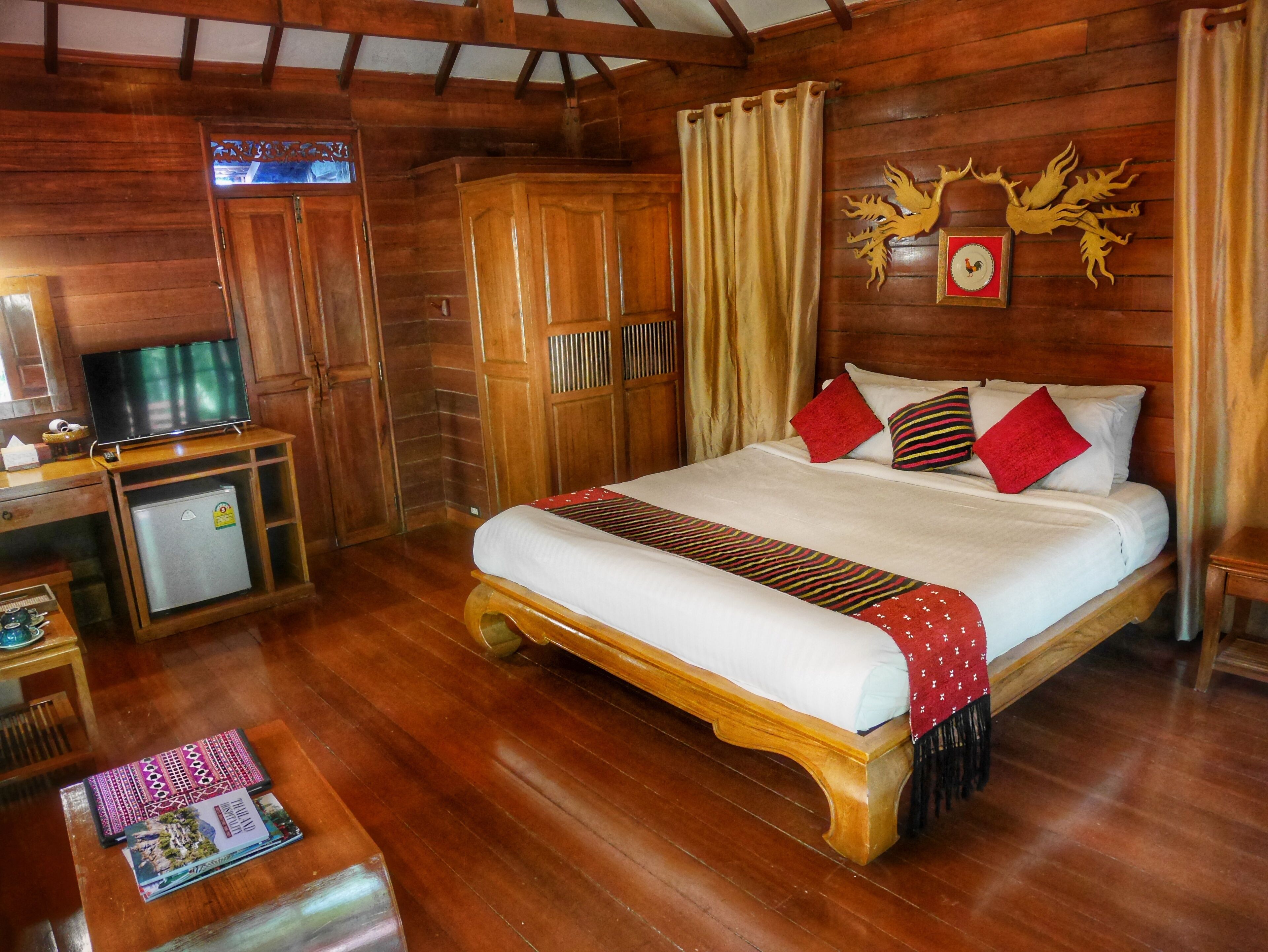 A wooden-themed hotel room with a bed, a television, a mini-fridge, and a wooden wardrobe.