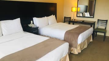 Ett hotellrum med två sängar, ett skrivbord, en stol, en lampa och en spegel.