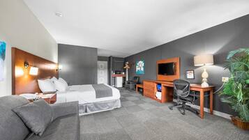 Una habitación de hotel con cama, escritorio, silla, televisor, lámpara y planta.