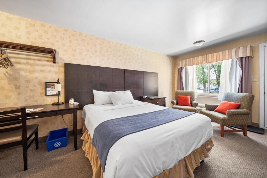 Quarto de hotel com uma cama grande, uma escrivaninha, uma cadeira e uma janela com cortinas.