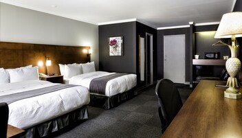 Habitación de hotel con dos camas, un escritorio, una silla, una lámpara, un microondas y una puerta que da a un baño.