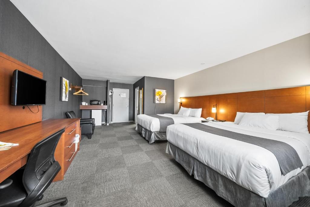 A hotel room with two beds, a desk, a chair, a television, and a wardrobe.