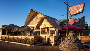 A wooden building with a thatched roof, a sign reading "Coconuts Bar", and a small stone structure in front. - Hotel - Motel Coconut (Trois-Rivieres)