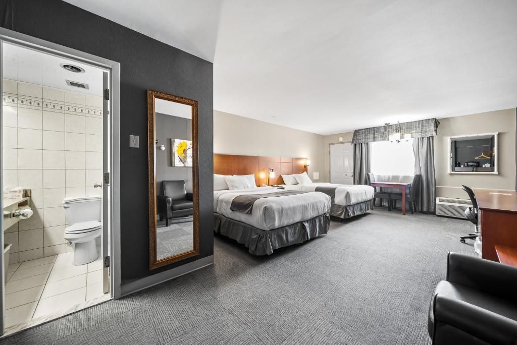 Ein Hotelzimmer mit zwei Betten, einem Badezimmer, einem Schreibtisch und einem Spiegel.