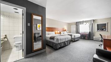 Ein Hotelzimmer mit zwei Betten, einem Badezimmer, einem Schreibtisch und einem Spiegel.