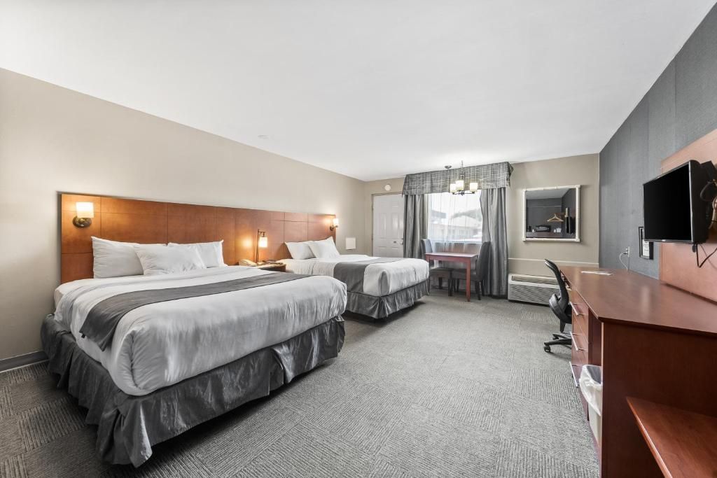 A hotel room with two beds, a desk, a chair, a television, and a window with curtains.