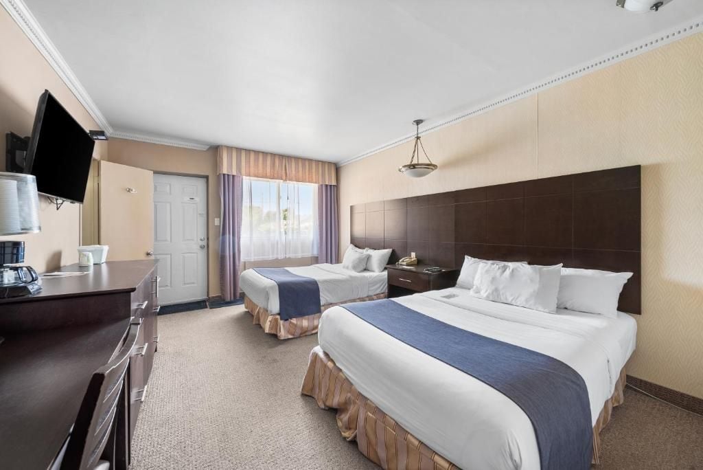 A hotel room with two beds, a desk, a television, and a window with curtains.