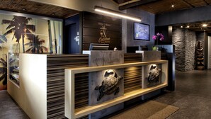 A reception desk with a wooden finish, a sign reading "Hotel - Motel Coconut," and a television screen above it. - Hotel - Motel Coconut (Trois-Rivieres)