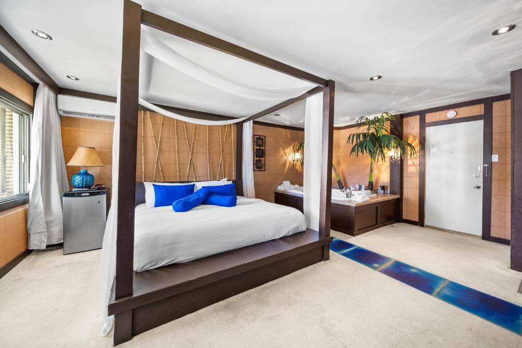 A four-poster bed with a canopy, a bedside table with a lamp, a small desk with a chair, and a door in a hotel room.