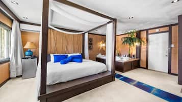 Un lit à baldaquin, une table de chevet avec une lampe, un petit bureau avec une chaise et une porte, le tout dans une chambre d’hôtel.