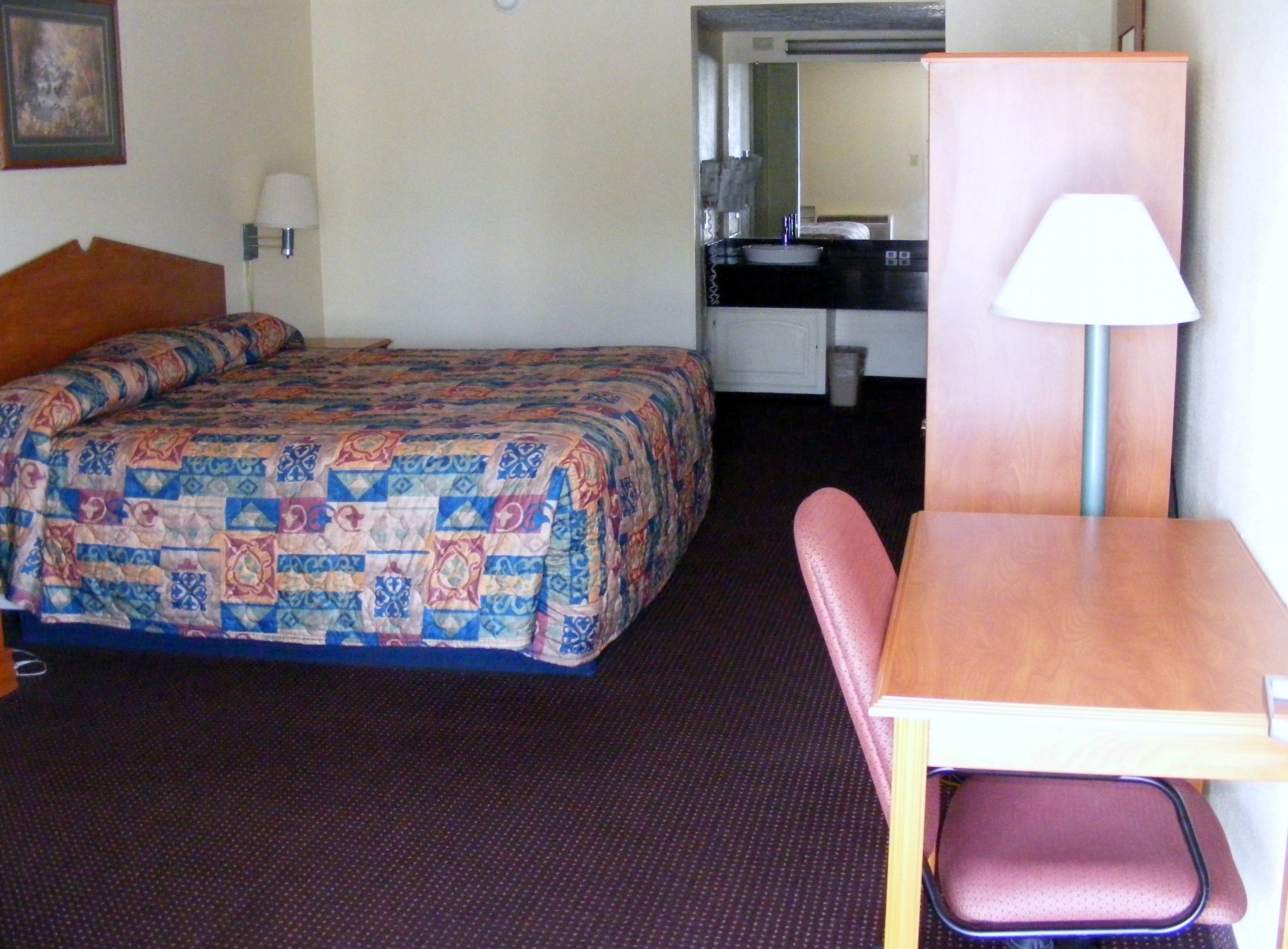A hotel room with a bed, a desk, a chair, and a lamp.