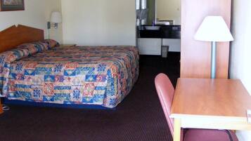 A hotel room with a bed, a desk, a chair, and a lamp.