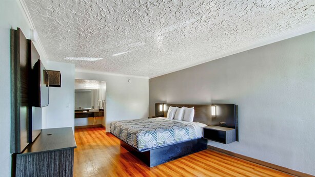 Une chambre moderne avec un grand lit, un plancher en bois, un plafond à la finition texturée et un téléviseur encastré dans le mur de gauche.