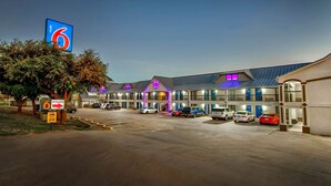 Un motel avec un grand panneau indiquant le chiffre « 6 », de nombreuses places de stationnement et une entrée bien éclairée.